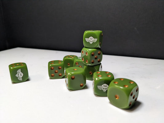 May include: A collection of olive green six-sided dice with metallic copper pips. Each die features a white graphic of a winged skull wearing a pilot cap on one face. The dice are arranged in a small stack and scattered across a flat surface.