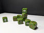 May include: A collection of olive green six-sided dice with metallic copper pips. Each die features a white graphic of a winged skull wearing a pilot cap on one face. The dice are arranged in a small stack and scattered across a flat surface.