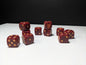 May include: A set of ten maroon six-sided dice with rounded corners. Each die features gold-colored pips, and one face on each die displays a detailed gold-colored engraving of a horned skull with flames, replacing the standard single pip.