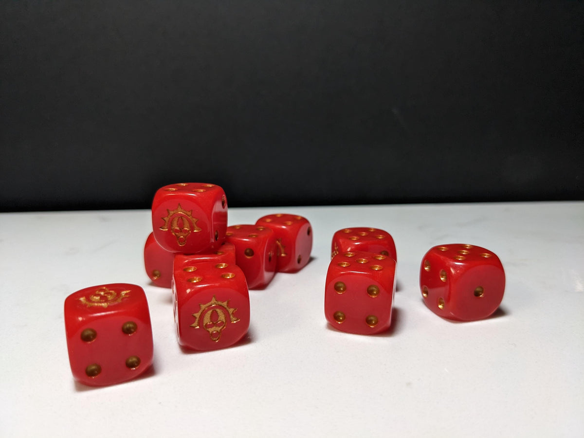 May include: A collection of eight red six-sided dice with gold-colored pips and a gold-colored emblem on one face of each die. The dice are arranged in a cluster, showing various sides with different numerical values and the custom emblem.